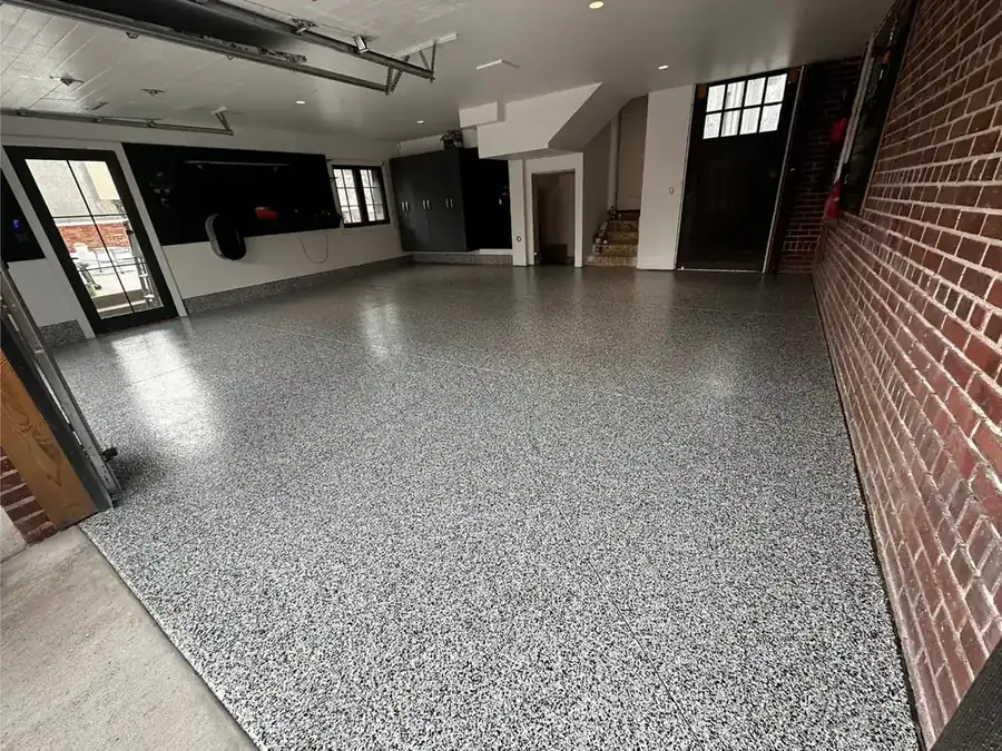 Gray flake polyaspartic garage floor beside a brick wall